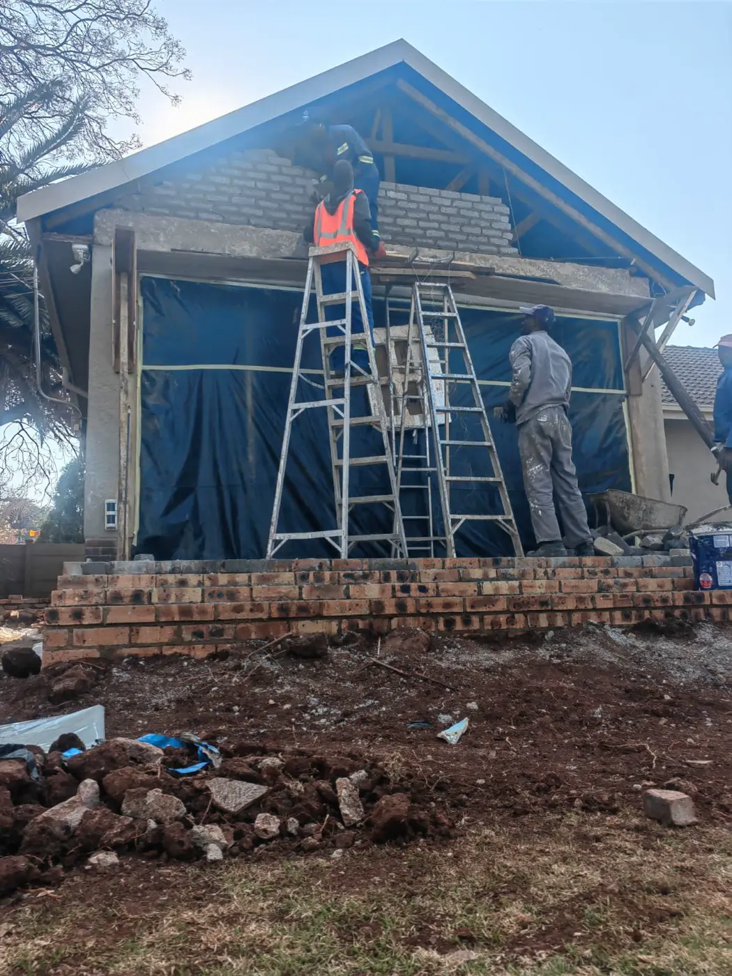 During: builders on ladders bricking up the new gable above the patio